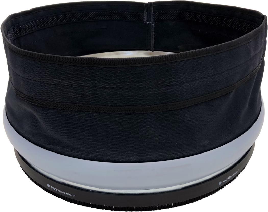 SPIDER ODSÁVACÍ MANŽETA (ABSAUGMANSCHETTE) Close-up view of the top rim and opening of a cylindrical black fabric container or hat. The image shows a circular inner opening with black lining, visible reinforced stitching and several horizontal fabric bands on the exterior. Near the lower edge there are two wide light-gray plastic rings and a black ribbed rubber base with small teeth and partially visible printed text 'Mink Flex-System®'. The fabric has a coarse weave and a matte finish; the object appears structured yet flexible. Lighting is even and the background is white.